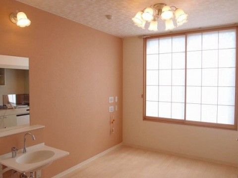 薄橙などの暖色を使用した居室。洗面台前の照明は室内灯と同じデザインで統一感がある。部屋の隅にはナースコールボタンが取り付けられている。