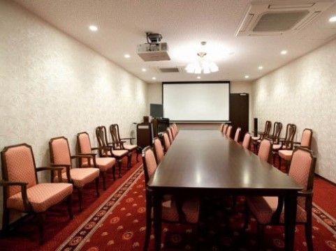プロジェクターとスクリーンの設置されたシアタールーム。赤い絨毯の上にテーブルと十分な数の椅子が用意されている。