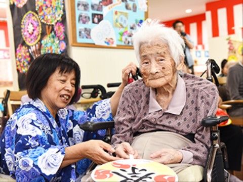 祭りの飾り付けがされた部屋で、車椅子に乗ってうちわを持っている女性
