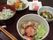 黒色のお盆に食事がのっている。たんぱく質や野菜が豊富なメニューで、おやつも付いている。箸には箸置きが使われている。