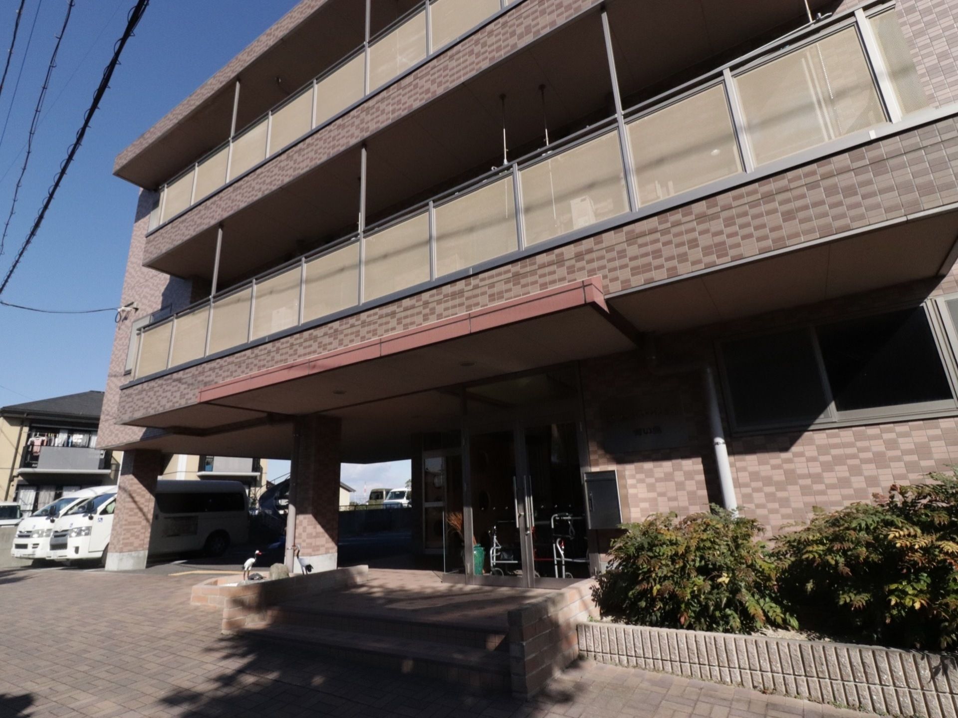 ３階建て。濃いベージュ系のタイル張りで、一般的な集合住宅と変わらない印象を与える。バリアフリーで段差がない。