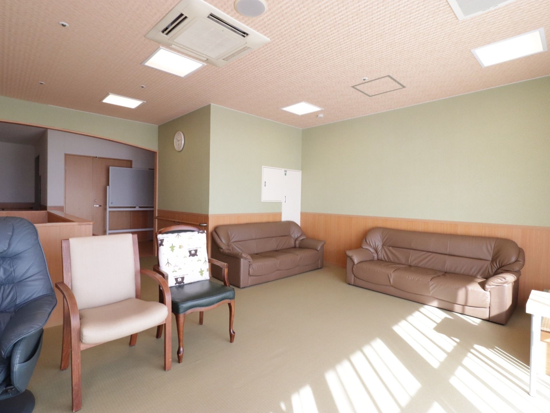 部屋の中に、茶色い３人掛けのソファが２台置かれている。また、椅子も数脚置かれている。奥にホワイトボードが見える。