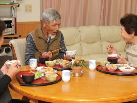 床に座ってテーブルを囲み、食事を楽しんでいる三人の入居者