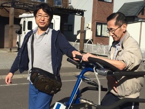 屋外にて、男性スタッフに付き添われながら、電動機器を使って歩行をする入居者
