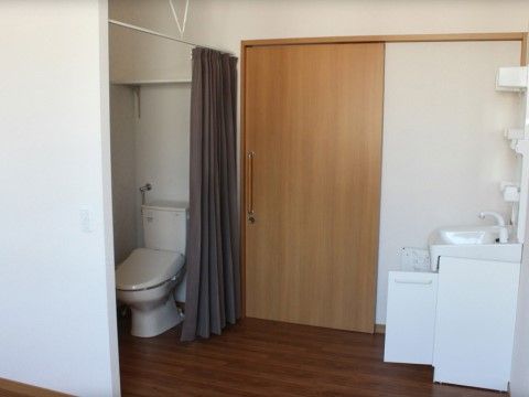 居室内のトイレはカーテンで仕切られておりプライバシーが確保されている。入口はスライドドアで車椅子をご利用の方でもスムーズに入室できる。