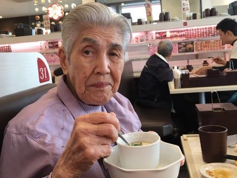 外出先の回転ずし屋のテーブルで、茶碗蒸しを片手に持っている女性入居者