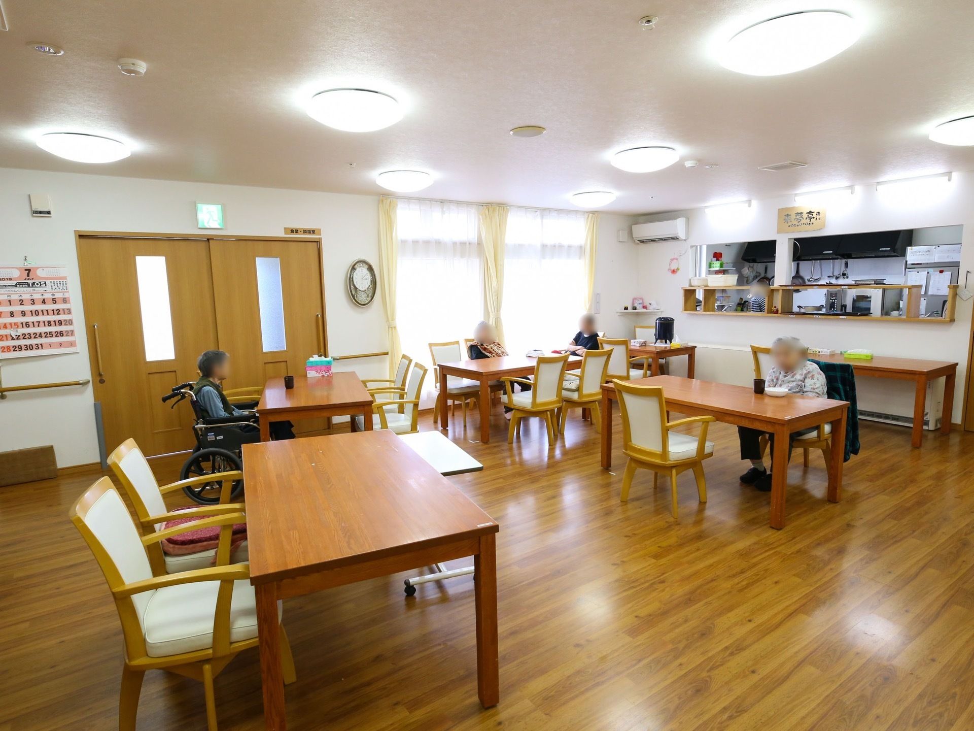 4人がけのテーブルがさまざまな向きに配置されている。薄い茶色の木枠の椅子のシートは薄いベージュである。