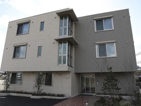建物の前に低木がいくつか植えられている、三階建ての施設外観
