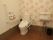ピンクと白のポップなデザインの壁紙が貼られたトイレには、温水洗浄便座器や手すり、呼び出しブザーが設置されている。