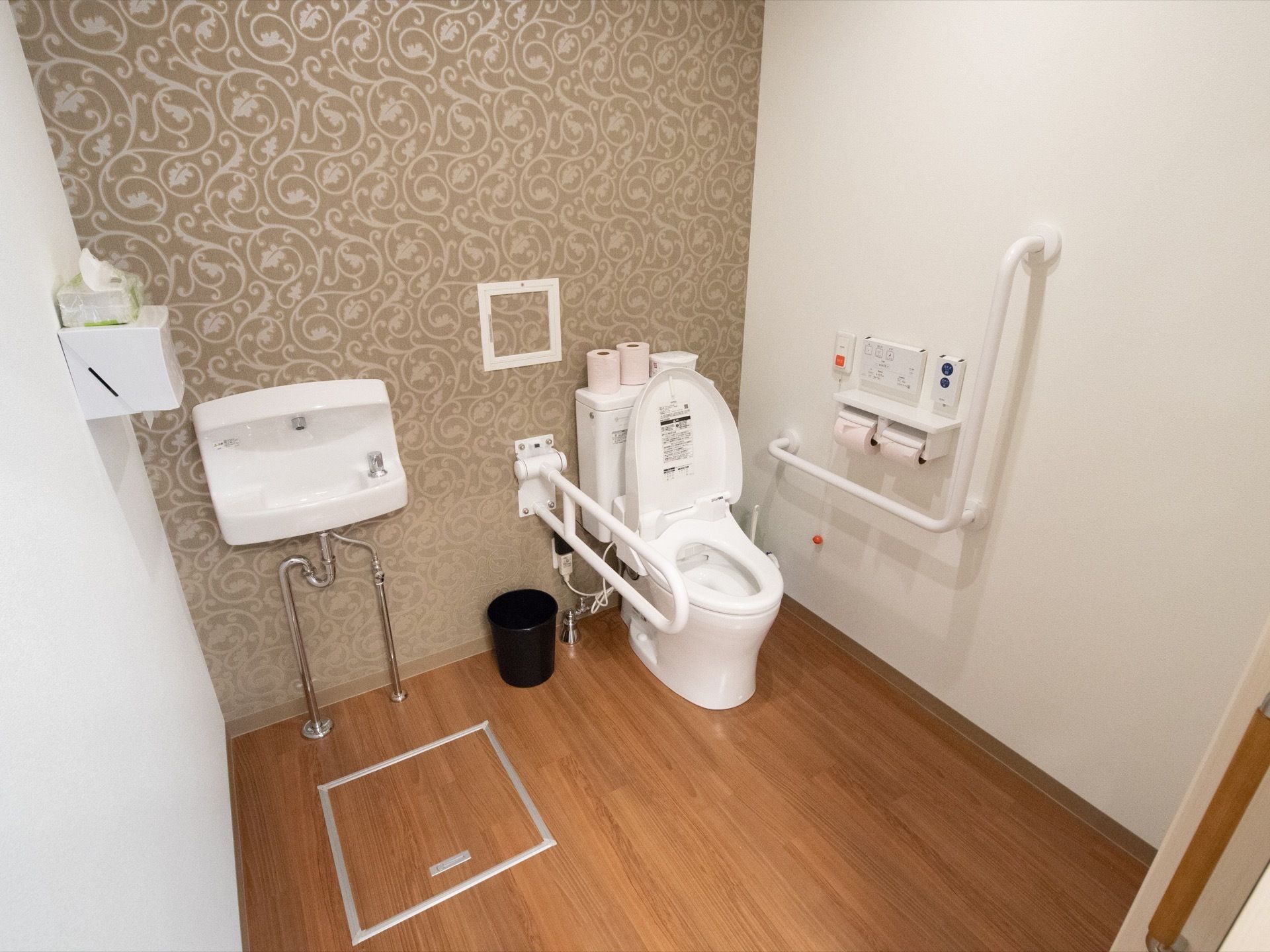 車椅子でも余裕のある広さのトイレがある。便座の周囲には手すりがついている。緊急時のためのスタッフコールもついている。