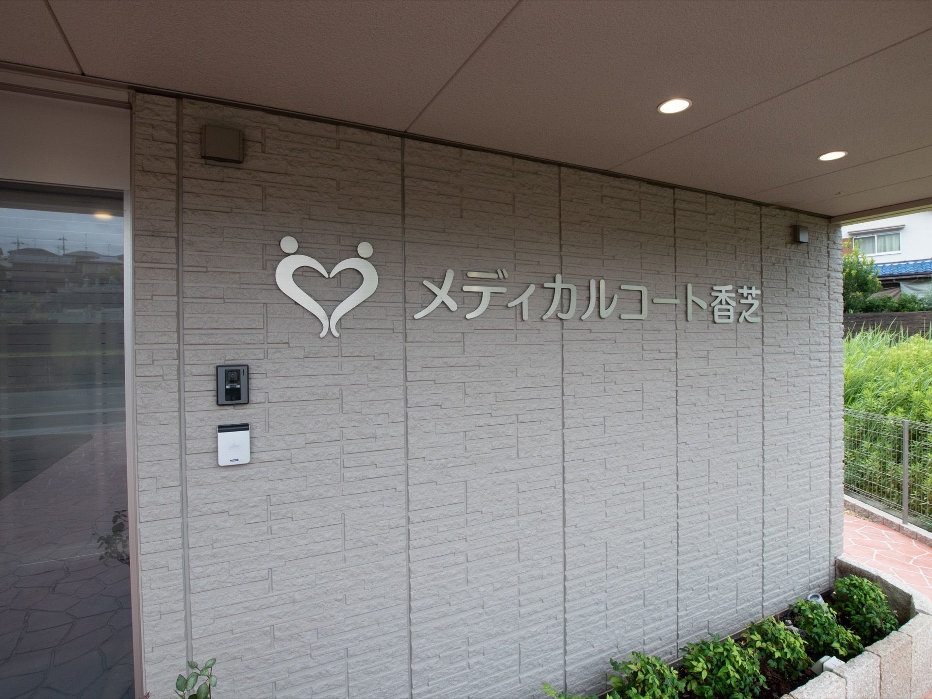 入口はタイルで舗装されている。扉の横にはインターホンがついている。壁にホームのロゴと名前が掲げられている。