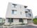 落ち着いたベージュ系の色合いの3階建ての建物である。外壁に施設名の看板が掲げられている。きれいに手入れされた植木がある。