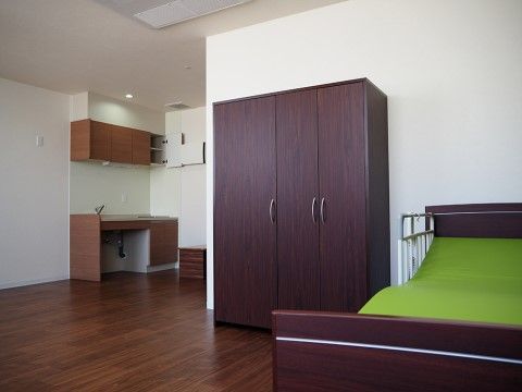 写真右手には緑のクッションの介護用ベッドが配置されており、その横には衣類などを収納できる大きなクローゼットが設置されている。