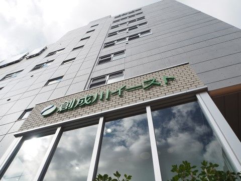 8階建てのグレーを基調とした建物で、1階の玄関部分はガラス張りの壁面となっている。上部には建物名が記載されている。