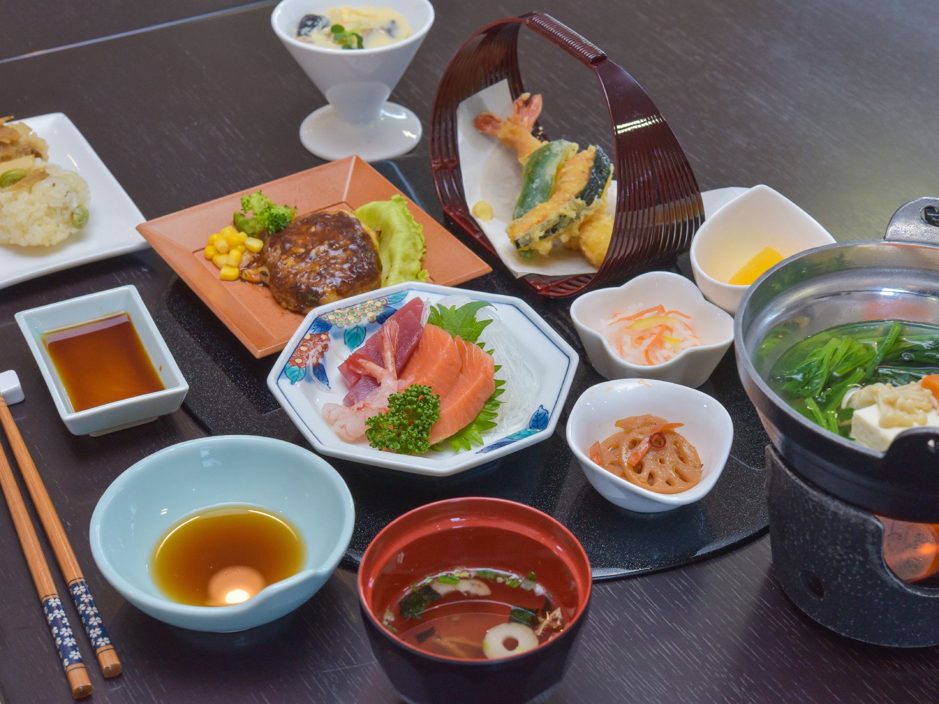 タケノコご飯のおむすびや鍋物、天ぷら、肉物、魚、野菜、汁物と品数豊富で見た目にも美しく並べられている。