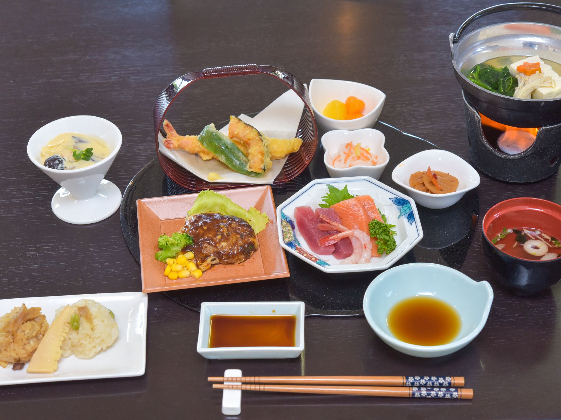 茶碗蒸しがある。野菜の天ぷら、酢の物、さしみ、ハンバーグとコーンなどと少量ずついろんなおかずが盆に盛り付けてある。