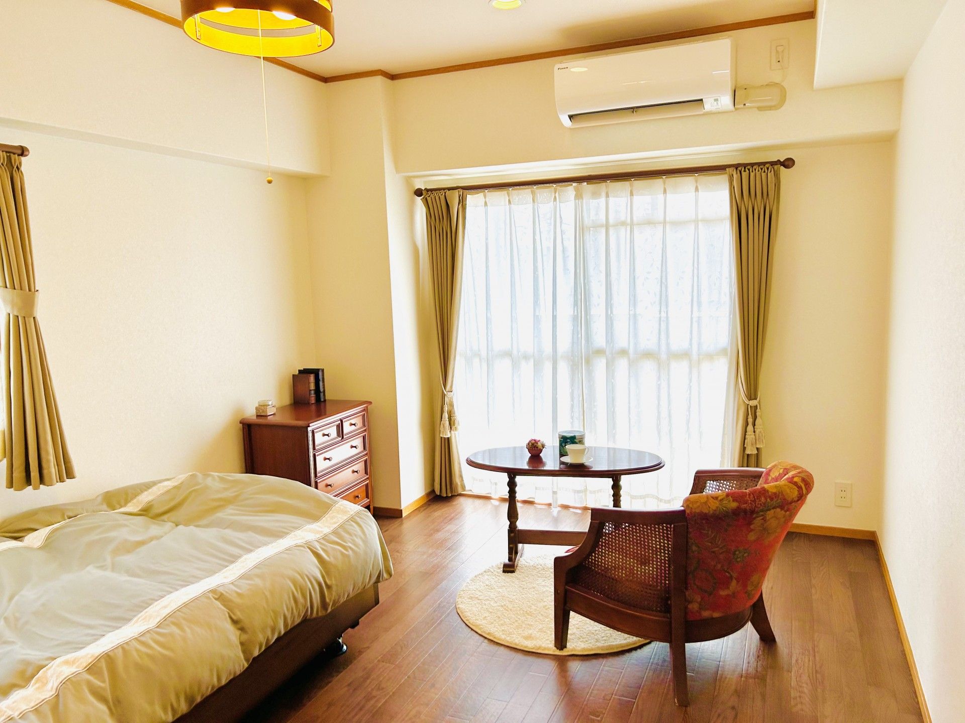白を基調とした部屋にベッドや家具が置かれている。床はフローリングになっており、扉は引き戸式になっている。