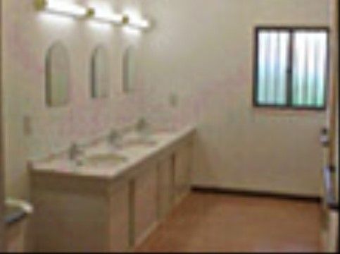 フラットなフロアの壁際に、白いシンクの洗面台が３つ並んで設置されている。その前の壁にはそれぞれ照明と鏡が備わっている。