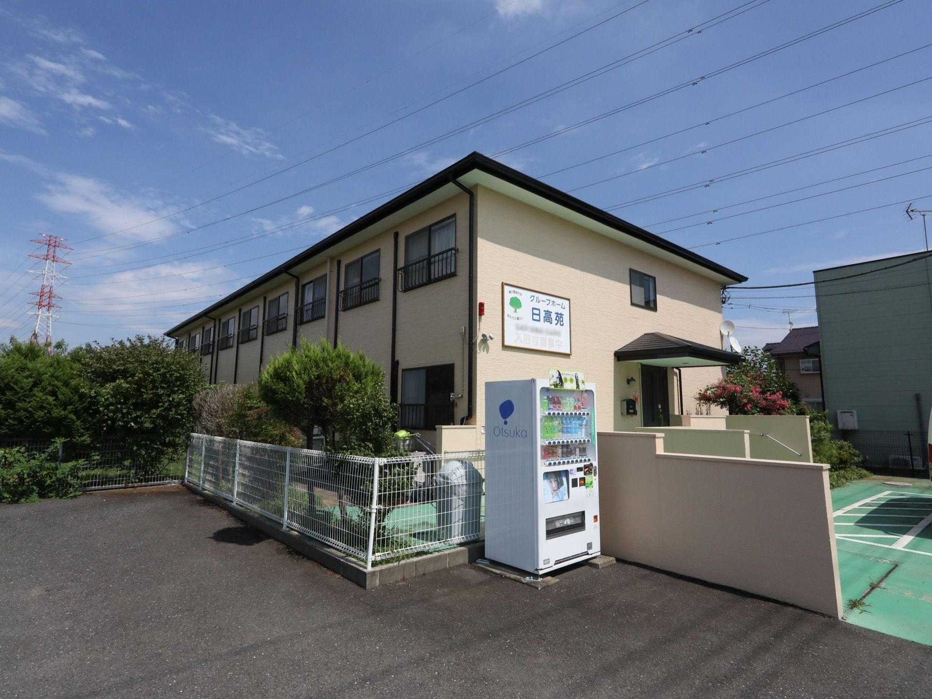 施設は横長の建物で、2階建てである。クリーム色の壁には、施設名を記載した看板が掲げられている。近くには飲み物の自動販売機がある。