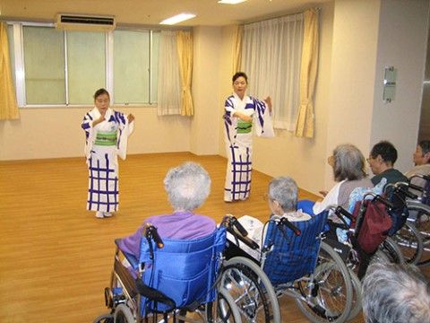 浴衣を着た二名の女性が踊っている様子を眺めている入居者たち