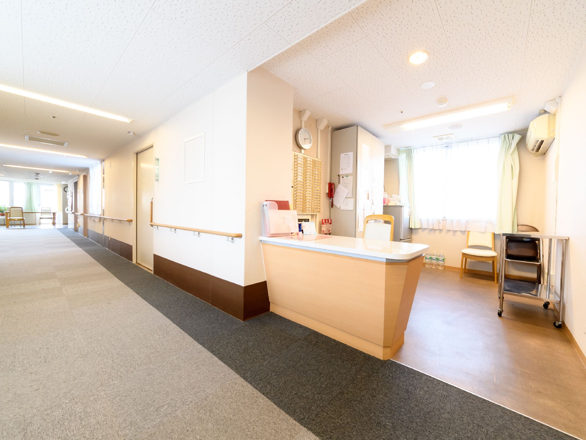 白く明るいフロア内である。壁面には手すりが取り付けられている。カウンターにはイスがひとつある。円形の掛け時計がある。