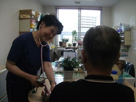 聴診器を付けた女性スタッフと、血圧を測ってもらっている男性入居者