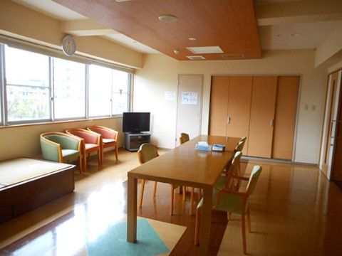腰高窓が並ぶ壁際に小上がりの畳スペースが設けられている。その横には１人掛けの椅子が３脚とテレビが設置されている。
