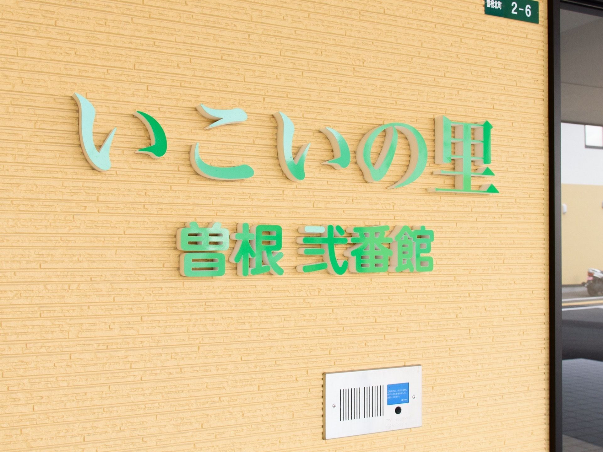 緑色の文字の施設名が、玄関脇のベージュ色の外壁に書かれている。大きな文字で遠くからでも見やすくなっている。