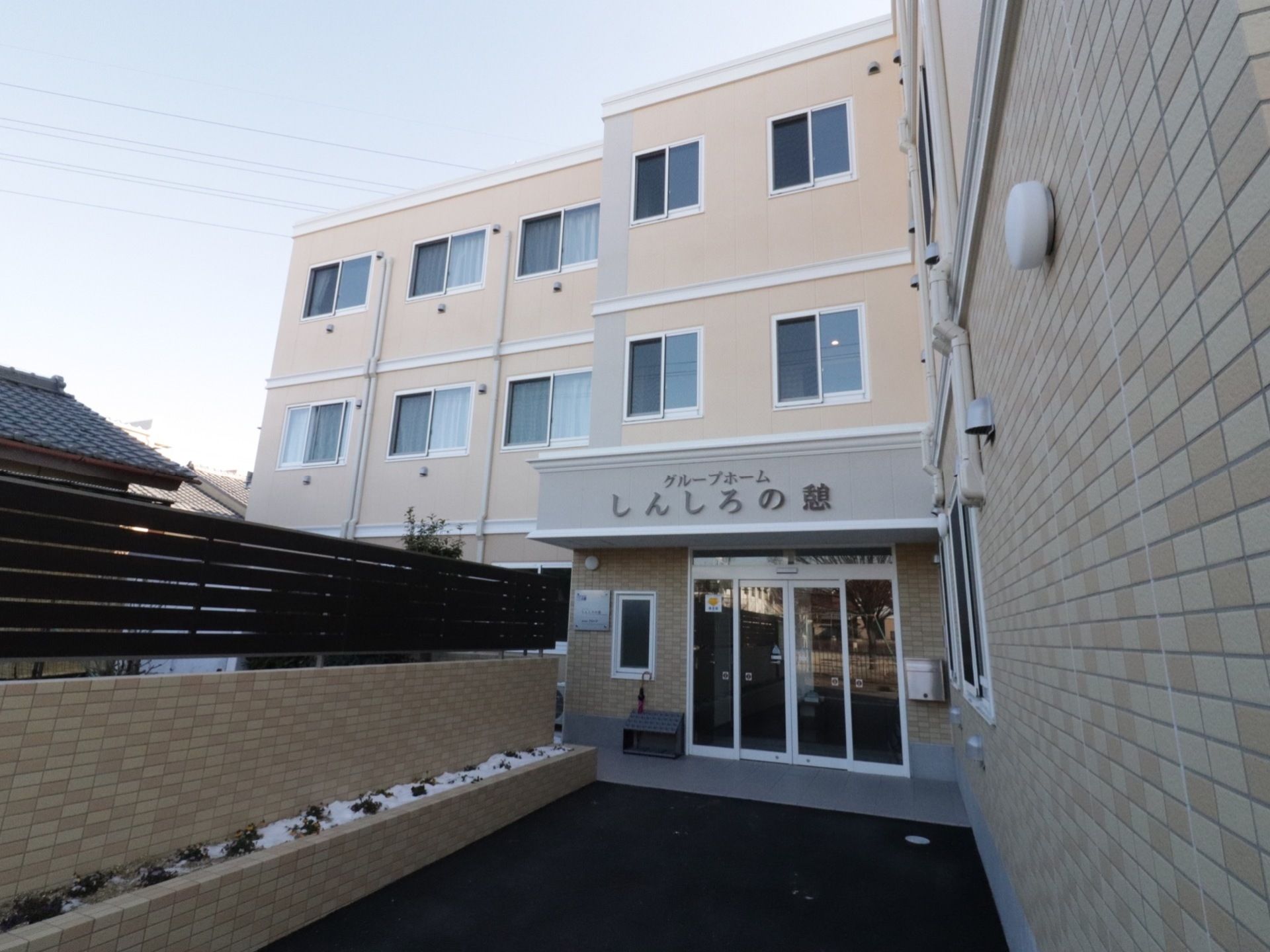 施設はベージュ系の壁で、３階建てである。玄関まではバリアフリーになっている。玄関ドアの上に施設名が書かれている。