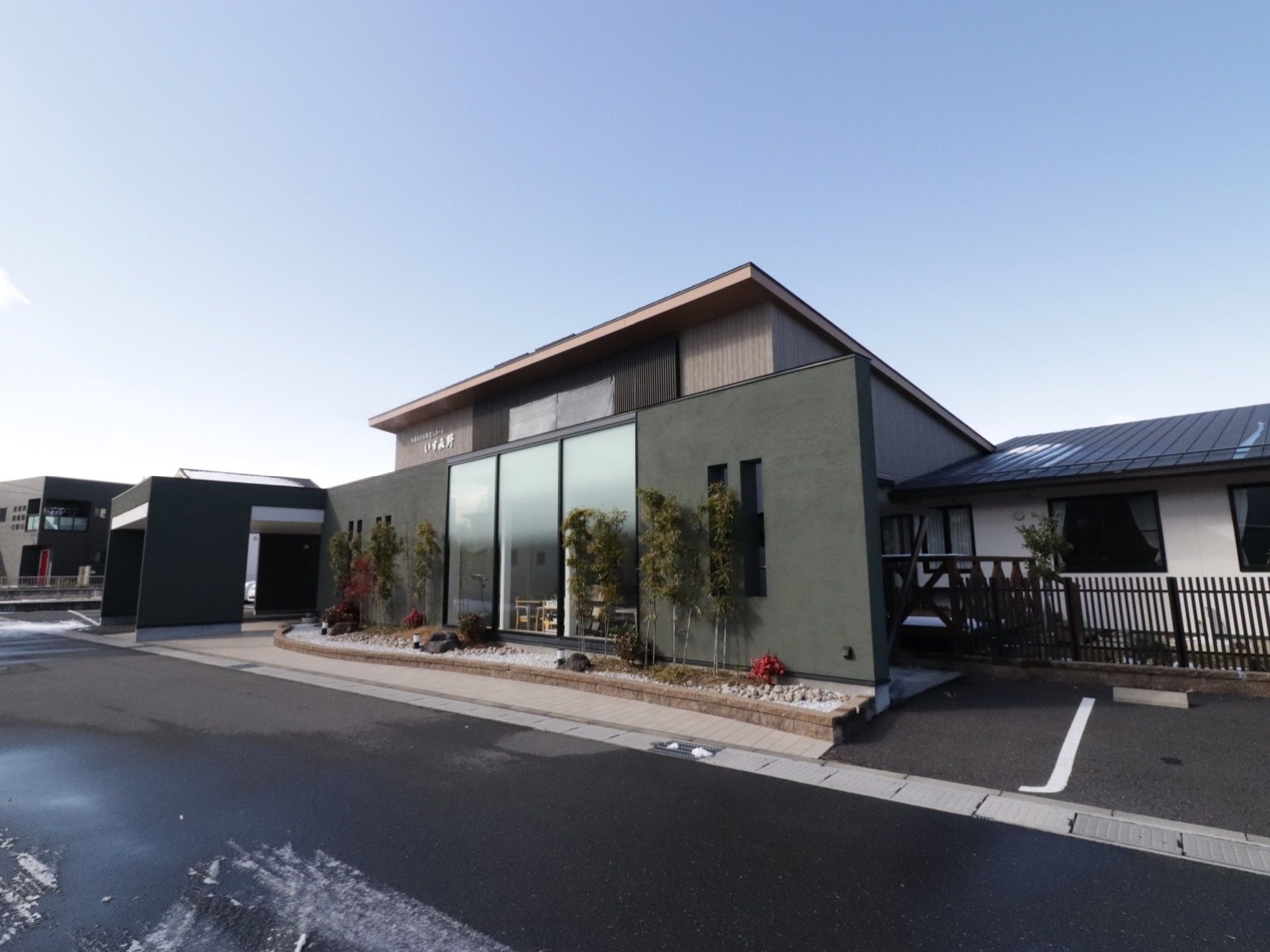 施設は平屋。道路に面して大きな窓が設置されている。建物の隣には駐車場がある。綺麗に手入れをされた植物が植えられている。