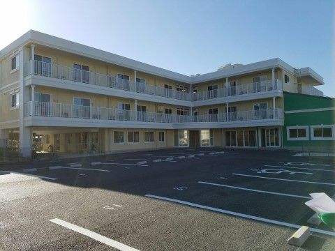ベージュ色の外壁の建物。一部に緑色の外壁のスペースがある。建物にはベランダがあり窓がたくさん付いている。