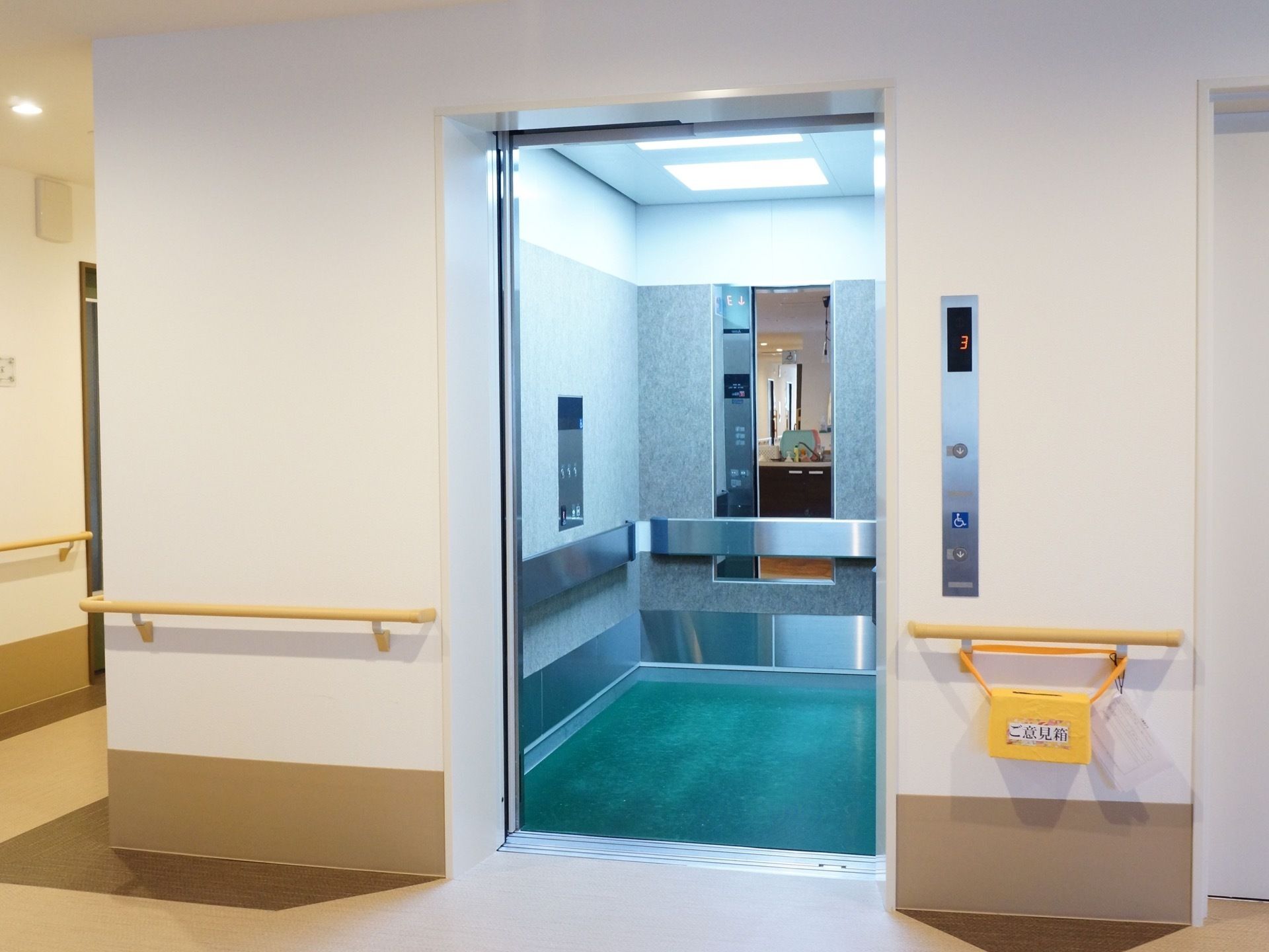 エレベーター内の照明は館内の物と違い、青白い光となっている。脇には入居者様の意見を投稿できる黄色い箱がある。