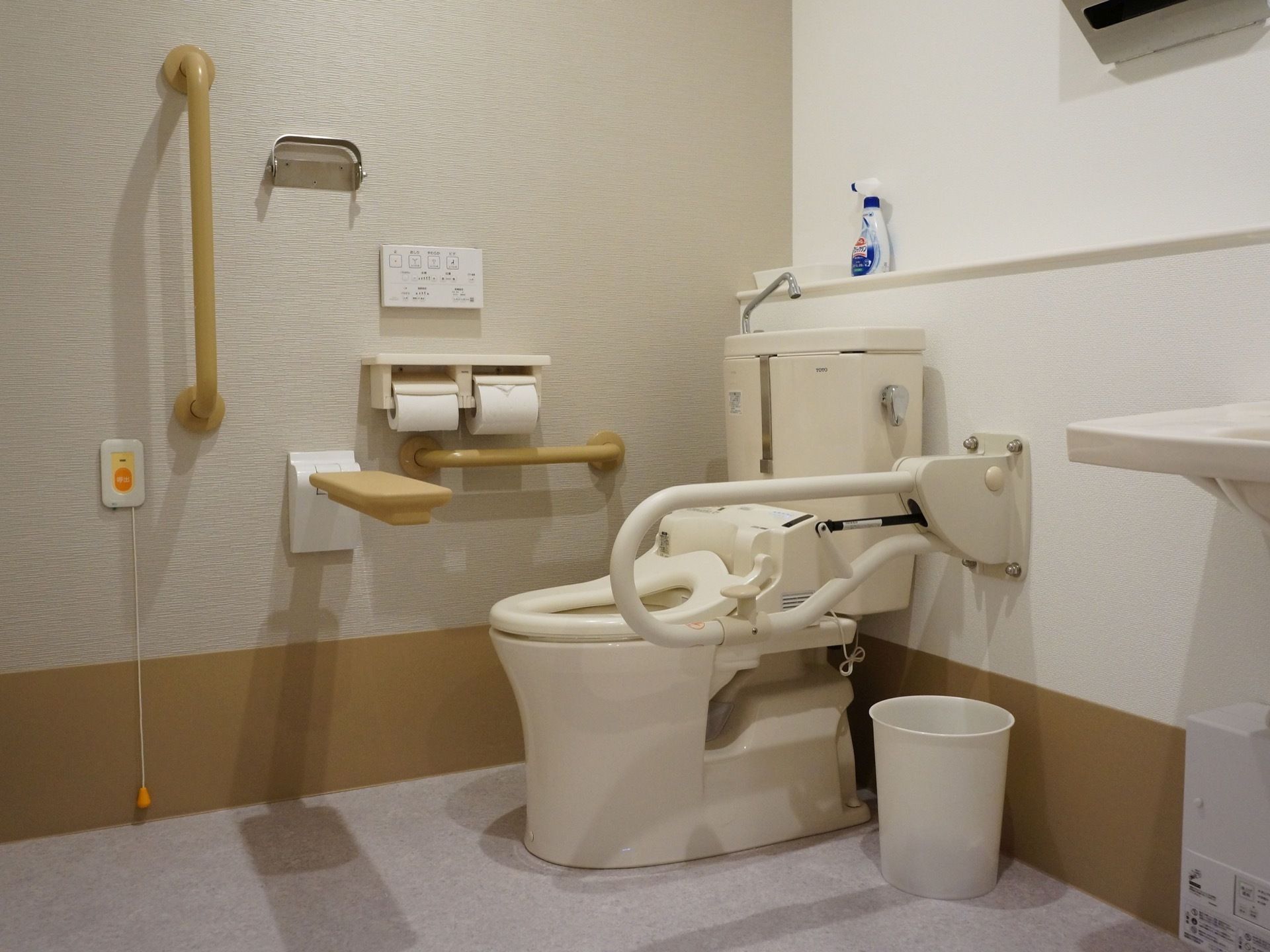 車椅子のままでも使用可能な広いトイレである。床はカーペットで、便器の周辺には折りたたみの手すりなどが設置されている。