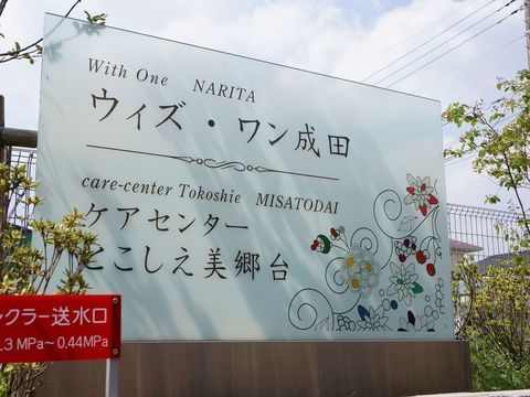 白地に花柄のイラストが描かれ、施設名が書かれている大きな看板