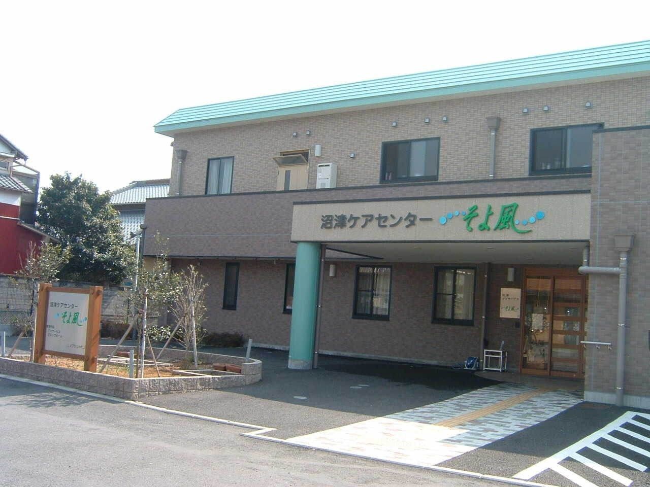 垣根の前に施設名の看板が設置され、駐車場が完備された施設