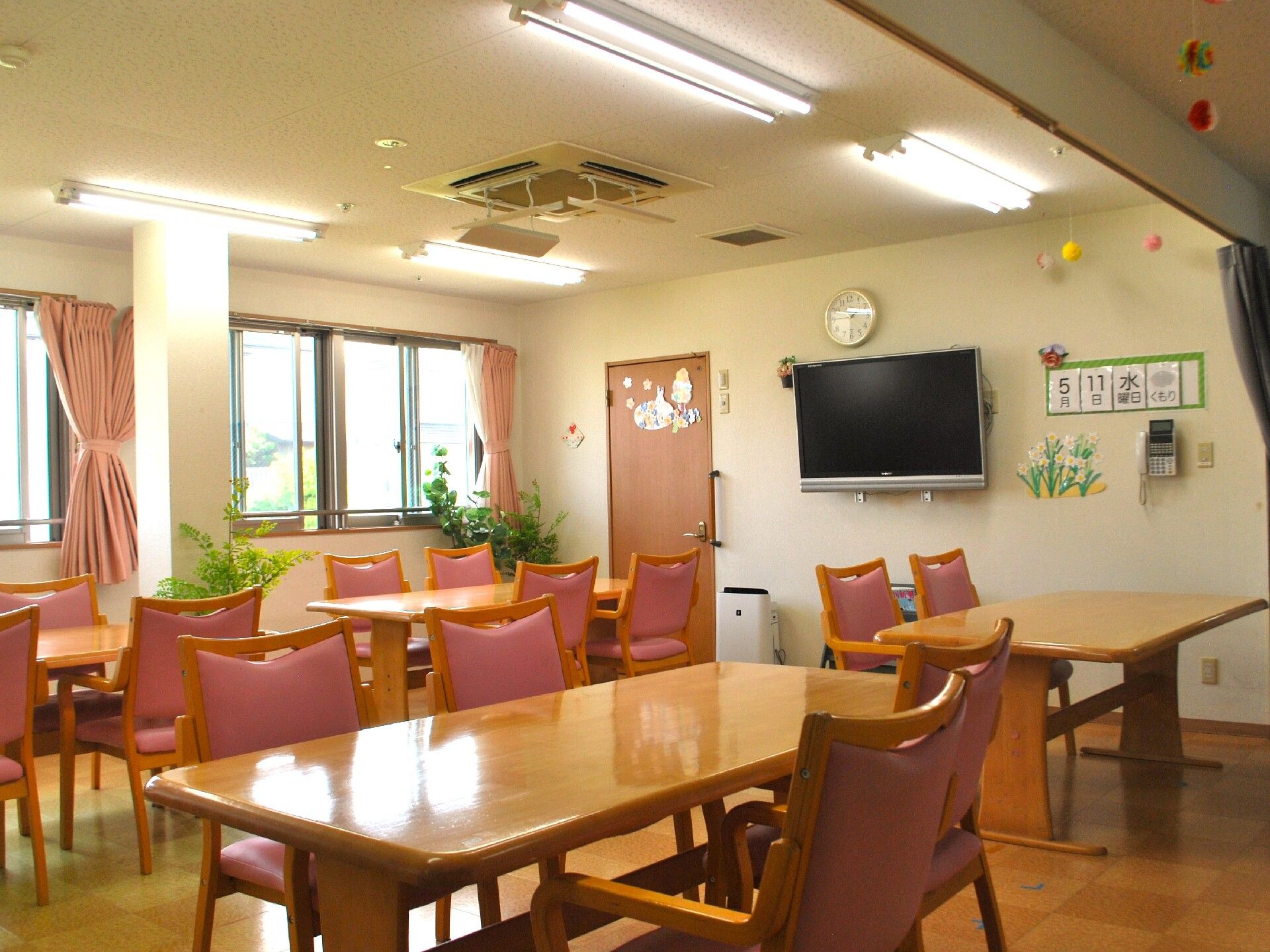 窓から光が入る明るい室内に、ダイニングセットが並んでいる。部屋までの廊下は、壁に手すりが付いている。