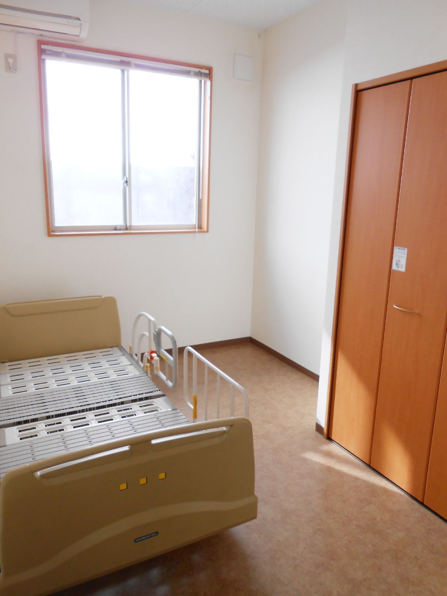 居室は個室制になっている。明るく落ち着いた雰囲気で、十分な広さがある。介護用ベッド、収納、エアコンが設置されている。窓が１か所ある。