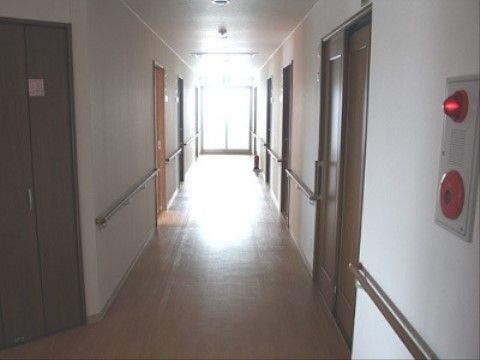 廊下は車椅子が通れる広さがあり、手すりも設置されている。突き当りには出入りができる窓ガラスがあり、その上に非常口の誘導灯が付いている。
