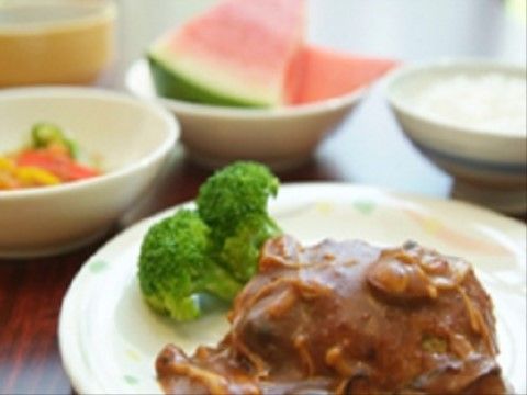 ブロッコリーが添えられ、きのこのデミグラスソースがかけられているハンバーグが主菜の食事