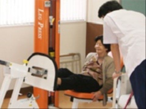 オレンジ色のリハビリ機器に座って、運動をしている入居者の女性