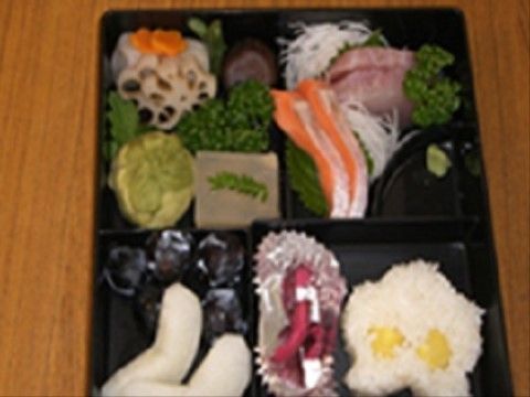 四つの仕切りがある和風弁当の中身は、お刺身、煮物、フルーツである。料理には季節の素材を使用している。