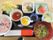 赤飯・刺し身・天ぷら・そばなど色とりどりの食事が、黒い盆の上に並んでいる。手前には袋に入った割り箸がある。