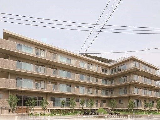 マンションのような外観の４階建ての建物。ベランダがぐるりと取り囲んでいる。カーテンの引かれた大きな窓が並んでいる。