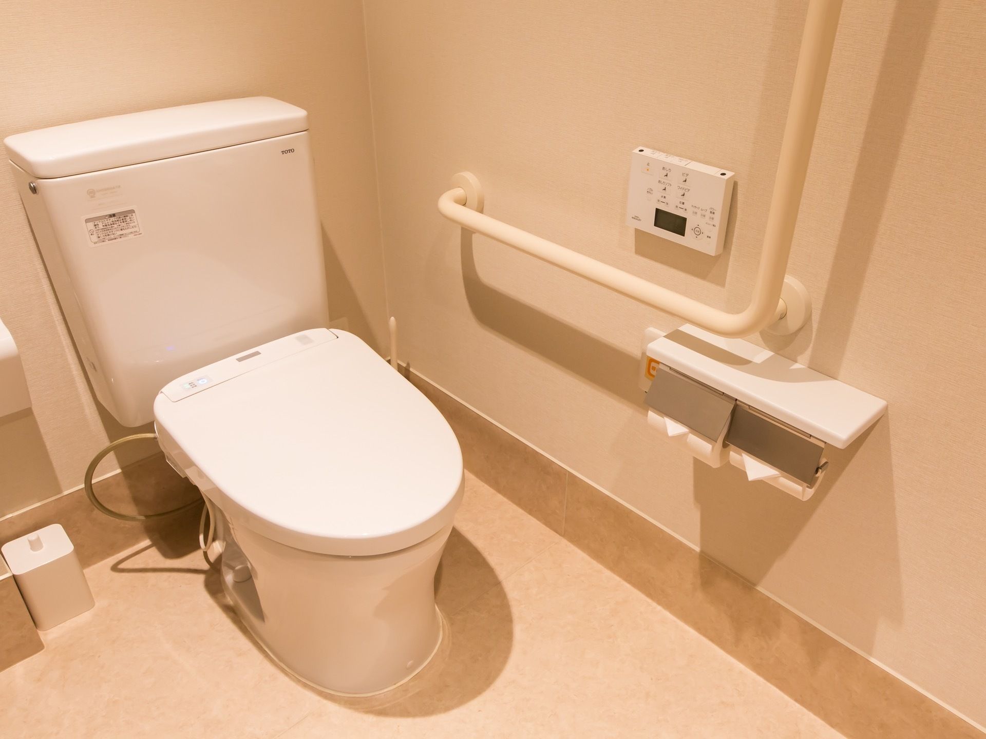 トイレは蓋つきの白色の便器である。洗浄暖房機能の操作パネルの近くに、Ｌ字型の手すりが設置されている。