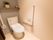 トイレの壁に、Ｌ字型の手すりが設置されている。便器の横には、跳ね上げ式の手すりがある。便座のふたにカバーがついている。