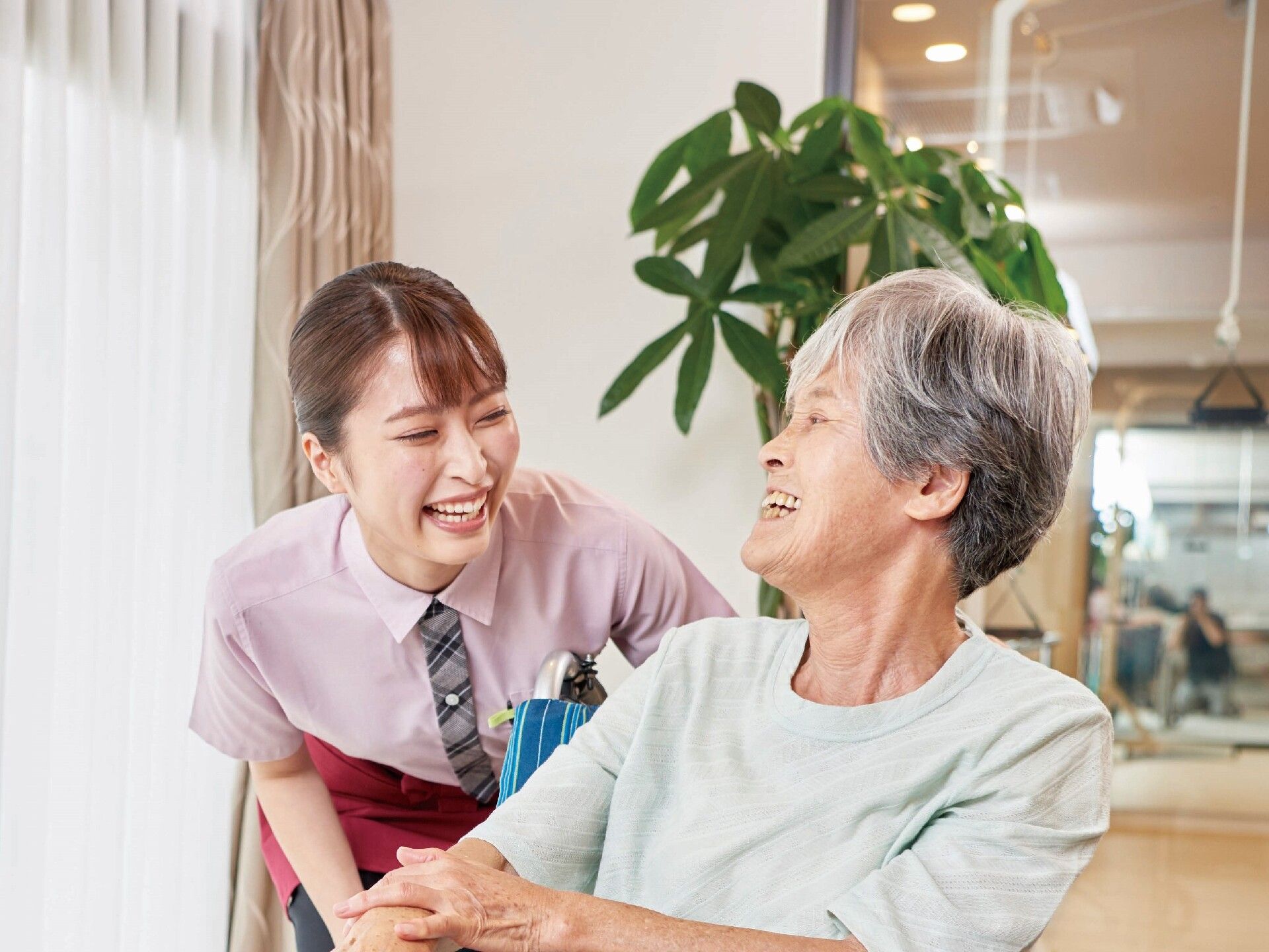 観葉植物の前にいる、笑顔の女性スタッフと車椅子の入居者