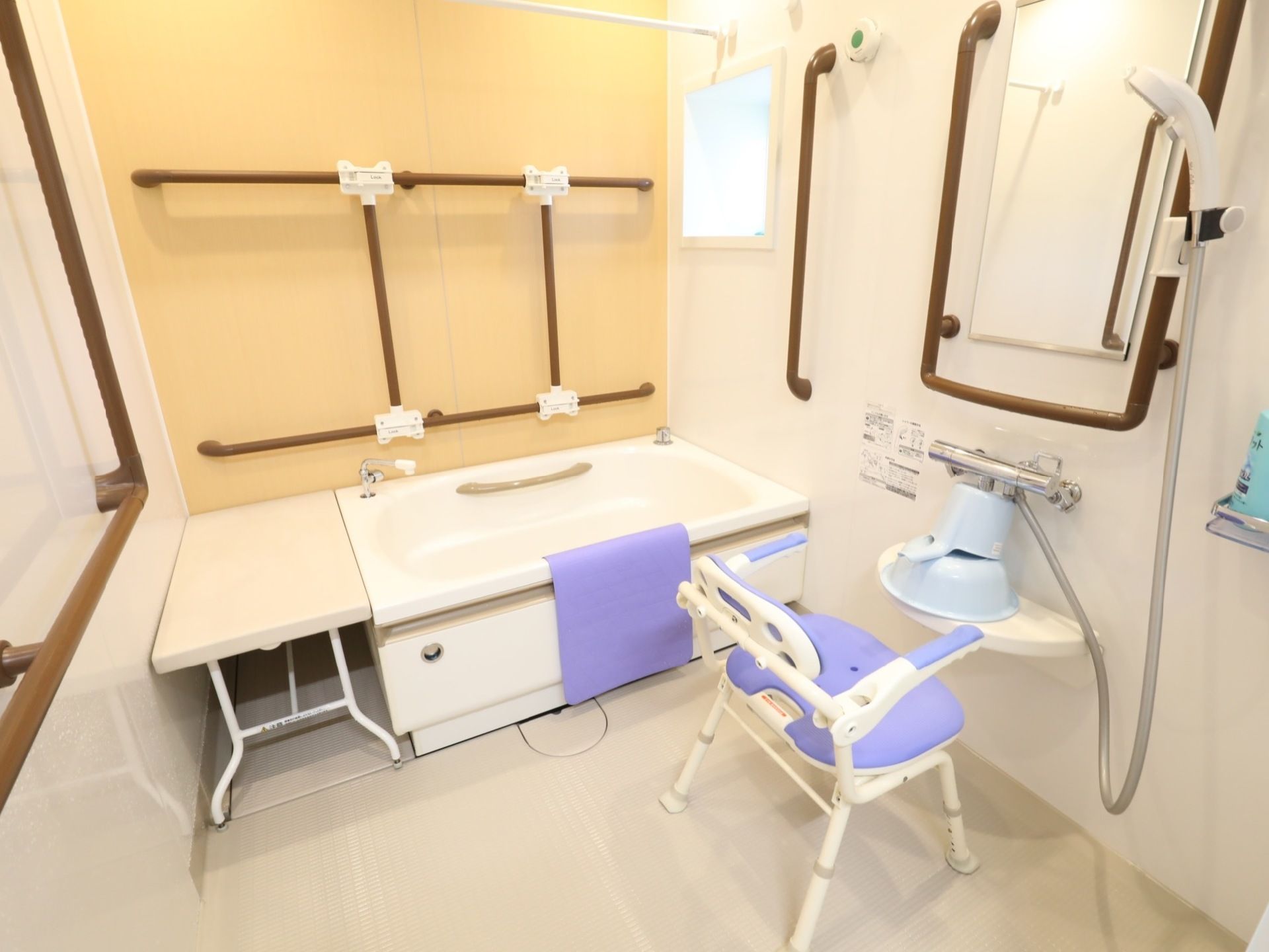 壁には茶色の手すりが数か所に設置されている。シャワーチェア置かれており、前の棚には洗面器や手桶が備えてある。