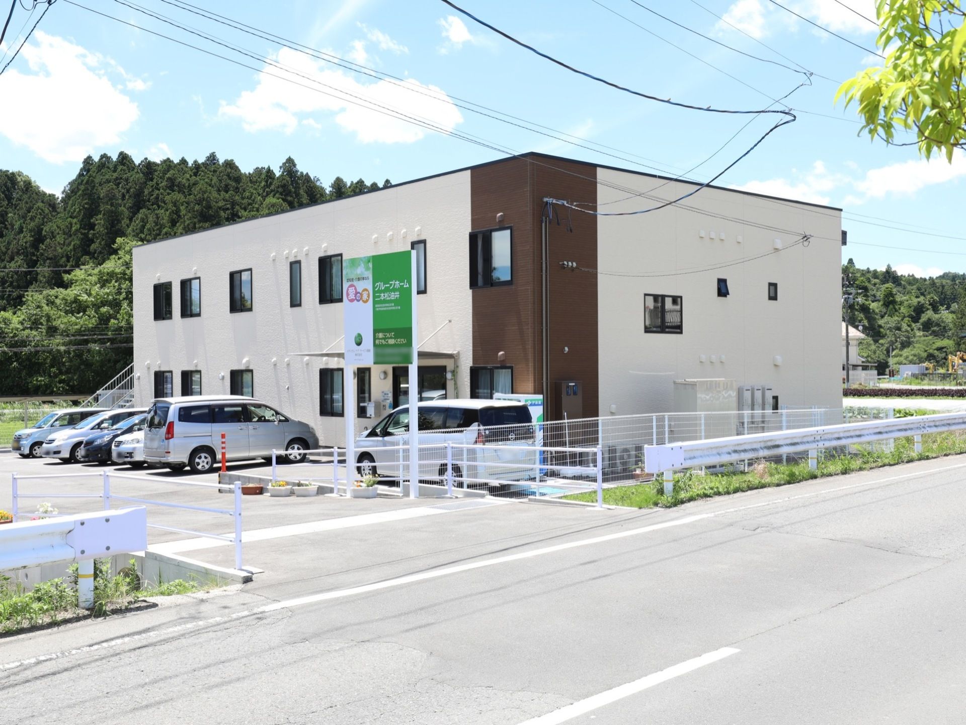 白と茶色の壁面になった2階建ての建物になっている。道路から施設へ入るところに、施設名が書かれた看板が設置されている。