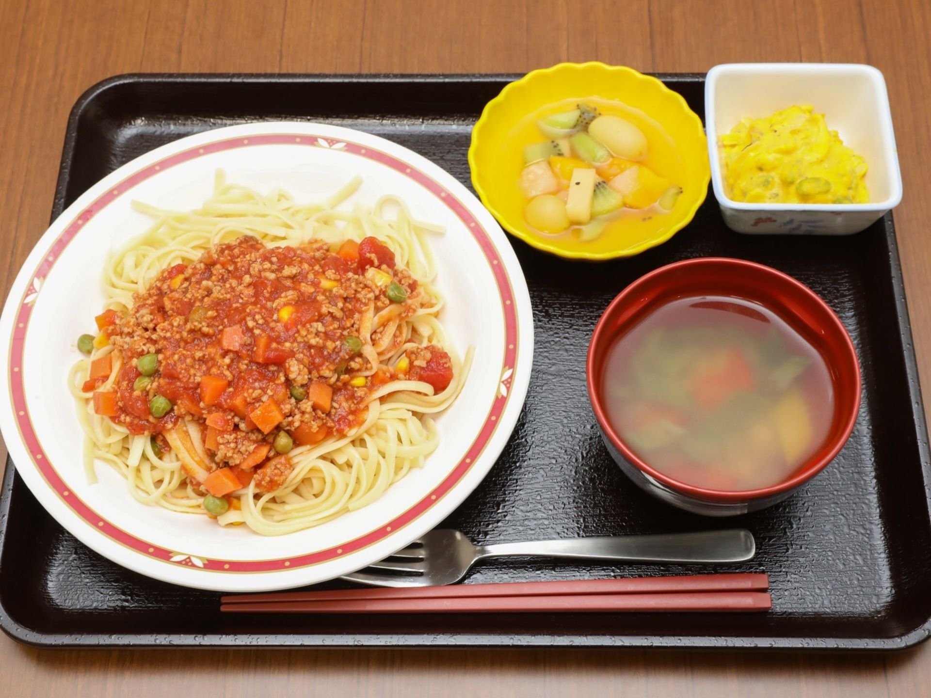 四角いトレーにスパゲッティーやスープ、フルーツなどが並べられている。お箸とフォークが用意されている。