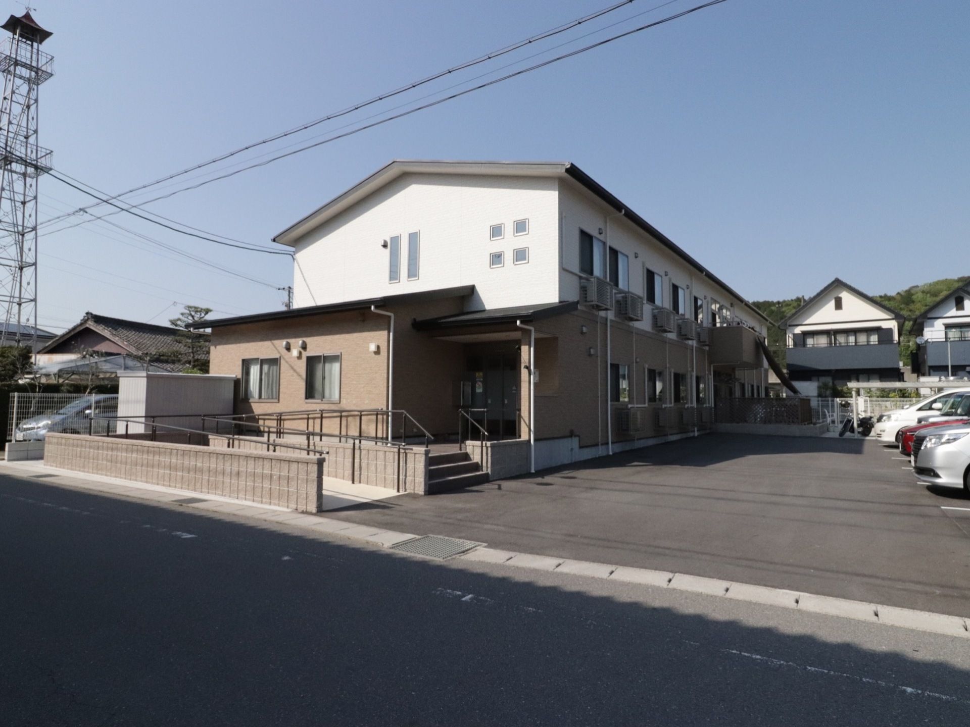 道路から施設の敷地へは、段差がない造りになっている。敷地の左側に施設の建物があり、右側に駐車場がある。